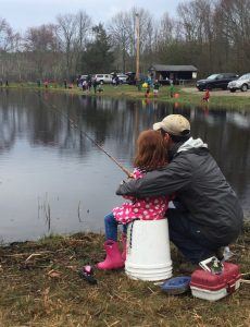 man with arms around daughter helping her fish