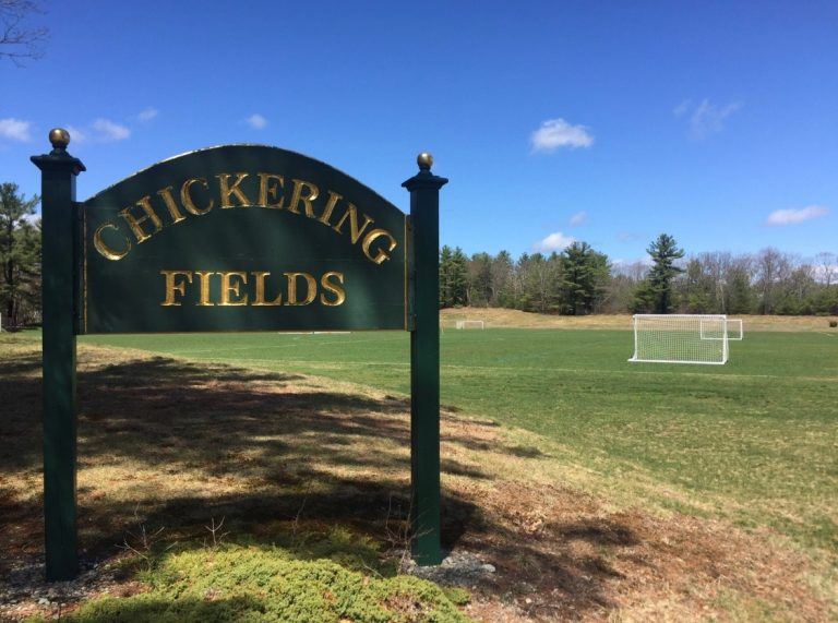 outdoor wooded sign reading chickering fields with grassy field behind