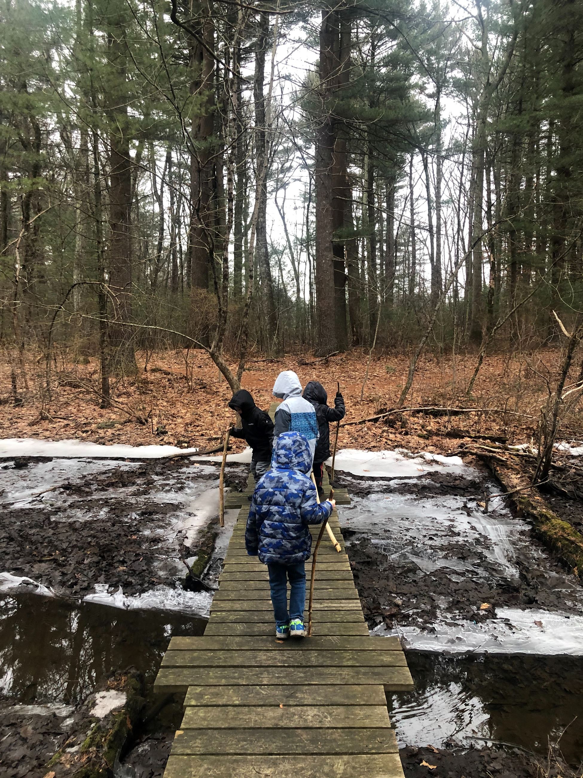 Photo of children walking over a bridge that has water and snow under it